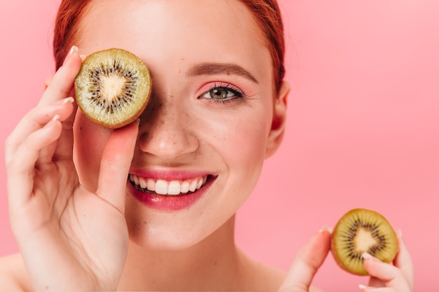 Close up view of blissful woman with kiwi. Studio shot of smiling female model with tropical fruits.