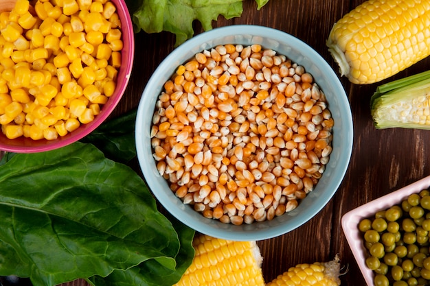 Close-up view of bowl full of corn seeds with spinach cooked corn seeds green peas on wooden table