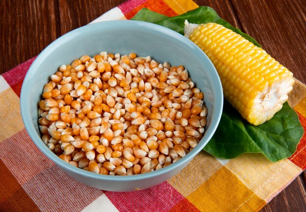 Close-up view of bowl with dried corn kernel and cooked corn with spinach on plaid cloth and wooden surface