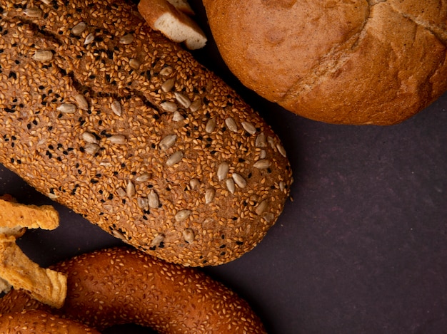 Close-up view of breads as bagel cob and baguette on maroon background with copy space