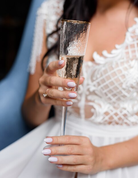 Close up view of bride holding a glass with champagne, without face