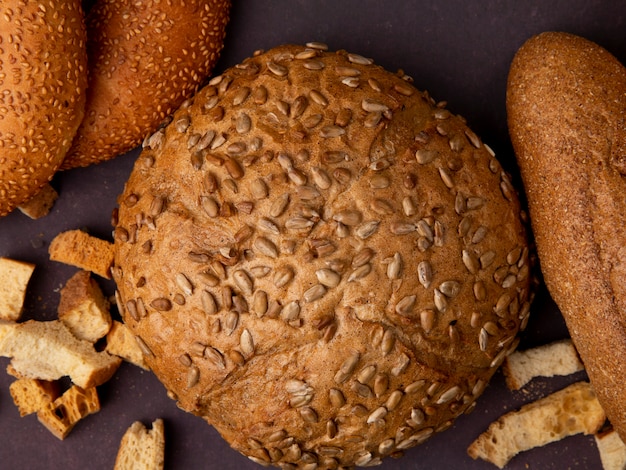 Free photo close-up view of brown seedy cob bread with bagels and baguette on maroon background