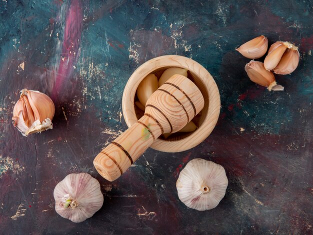 Close-up view of bulbs and cloves of garlic with garlic crusher on green and maroon background with copy space