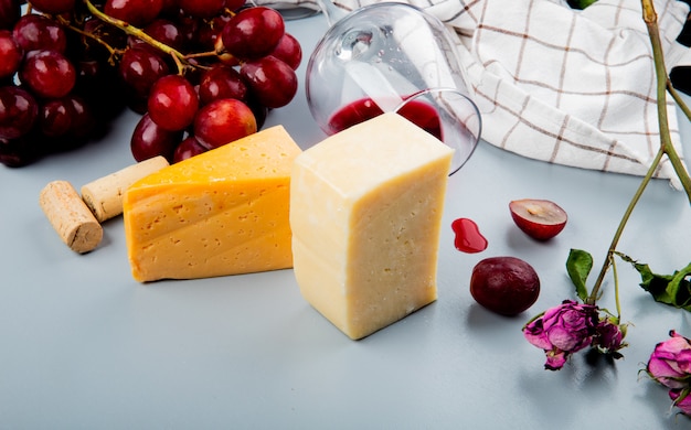 Close-up view of cheese and glass of red wine and grape with corks and flowers on white