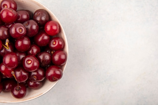 Close-up view of cherries in bowl and on white background with copy space