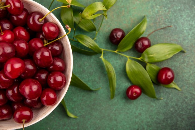 Close-up view of cherries in bowl with leaves and cherries on green background