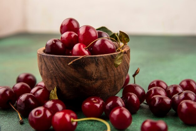 Close-up view of cherries in wooden bowl and on green surface and white background