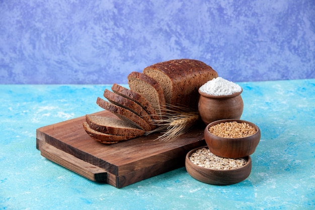 Close up view of chopped in half black bread slices on wooden boards flour wheat oatmeal in bowls on light ice blue pattern background