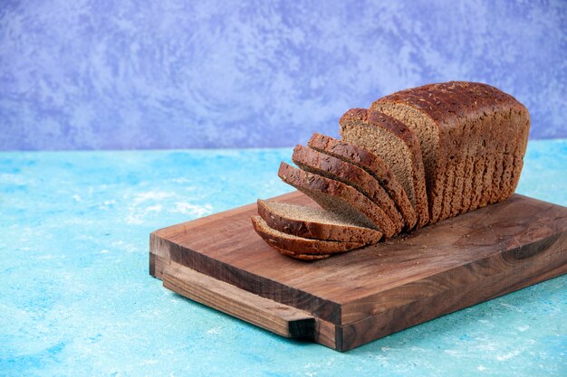 Close up view of chopped in half black bread slices on wooden boards on the left side on light ice blue pattern background