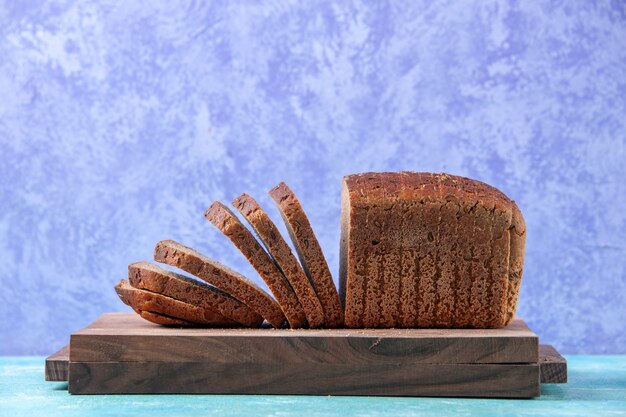 Close up view of chopped in half black bread slices on wooden boards on light ice blue pattern background