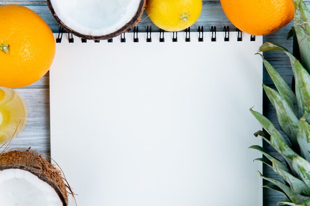 Close-up view of citrus fruits as orange coconut tangerine pineapple lemon with note pad on wooden background with copy space