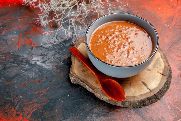 Close up view of classic tomato soup in a blue bowl spoon on wooden tray on mixed color table