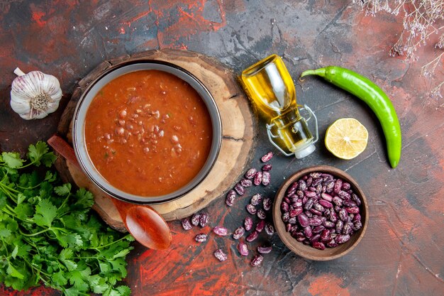 Close up view of classic tomato soup in a blue bowl spoon on wooden tray oil bottle garlic salt and lemon a bunch of green on mixed color table