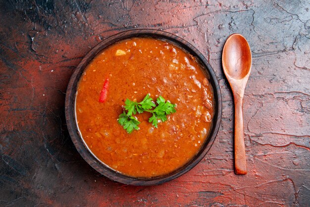 Close up view of classic tomato soup in a brown bowl and spoon on mixed color table