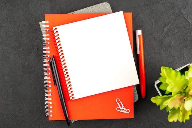 Free photo close up view of closed spiral notebooks in different sizes and pens flower pot on black