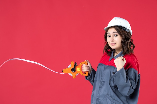 Free photo close up view of confident female architect in uniform with hard hat opening measuring tape on red wall