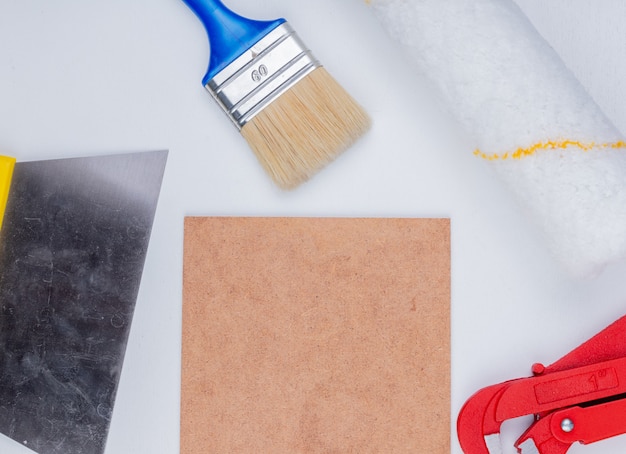 Close-up view of construction tools as paint brush and roller pipe wrench putty knife around mettlach tile on white background