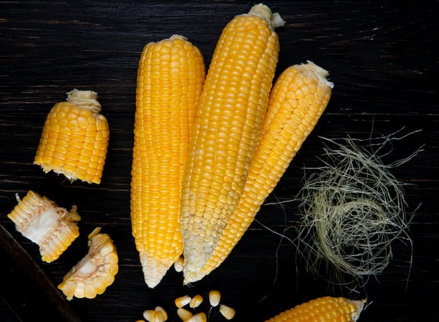 Free photo close-up view of cooked whole and cut corns with corn silk on black surface