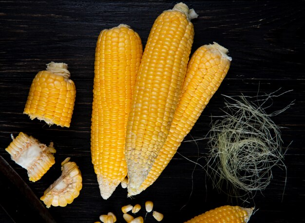 Close-up view of cooked whole and cut corns with corn silk on black surface