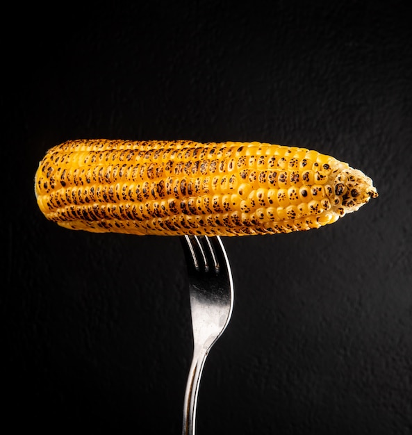 Close-up view of corn cob with fork on black wall