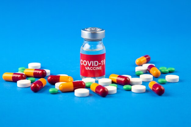 Close up view of COVID- vaccine in medical ampoule pills capsules on dark and soft blue background