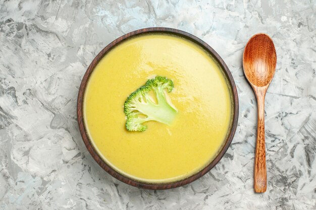 Close up view of creamy broccoli soup in a brown bowl and spoon on gray table