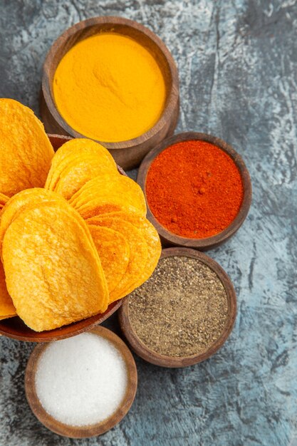 Close up view of crispy chips on wooden cutting board served with different spices mayonnaise and ketchup on gray table