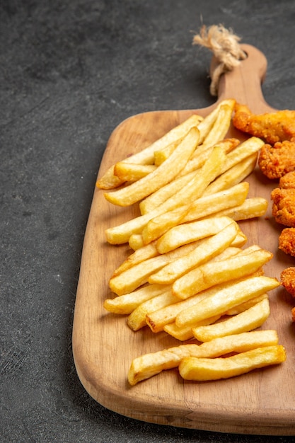 Close up view of crispy and fried chicken meal on wooden cutting board on dark