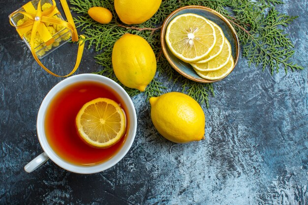 Close up view of a cup of black tea with lemon and collection of half whole citrus fruits on fir branches gift boxes on dark background