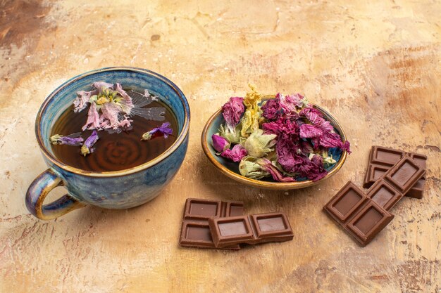 Close up view of a cup of hot herbal tea and chocolate bars on mixed color table