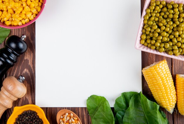 Close-up view of cut corn with corn seeds black pepper seeds green peas spinach and note pad on wooden surface with copy space