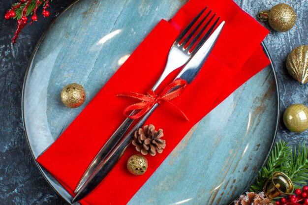 Close up view of cutlery set with red ribbon and decorative napkin on blue plate decorative accessories on dark background