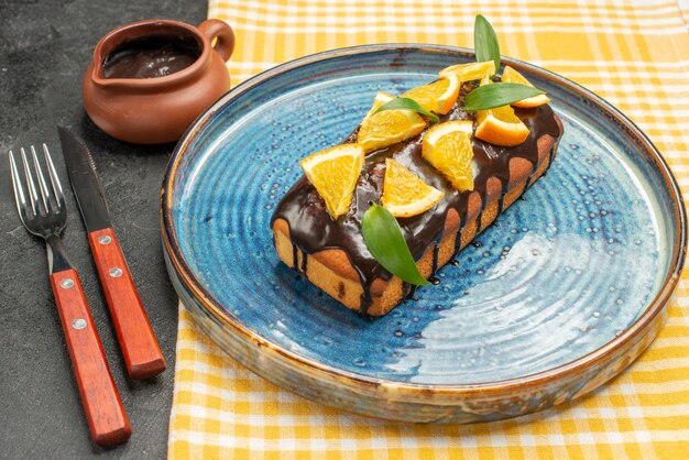 Close up view of delicious cake decorated with orange and chocolate served with fork and knife