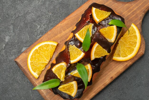 Крупным планом вид вкусных тортов, украшенных апельсином и шоколадом на разделочной доске на черном столе