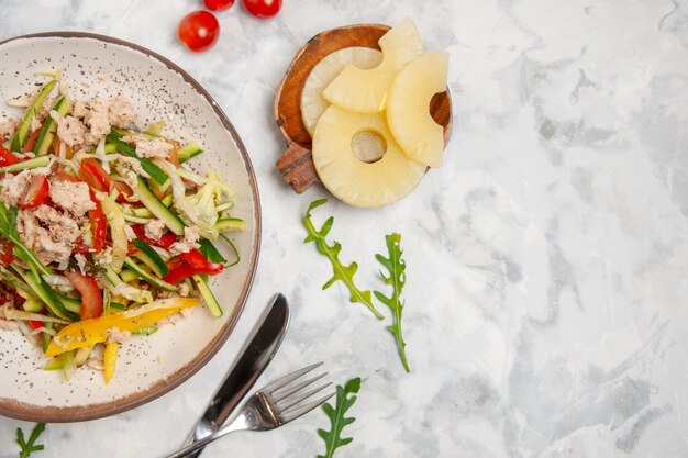 Close up view of delicious chicken salad with vegetables tomatoes dried pineapples cutlery set on the right side on stained white surface