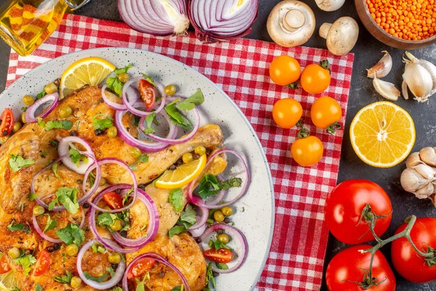 Close up view of delicious dinner fried chicken dish with various spices and foods tomatoes with stems red lentil garlics fallen oil bottle lemon mushrooms on dark color background