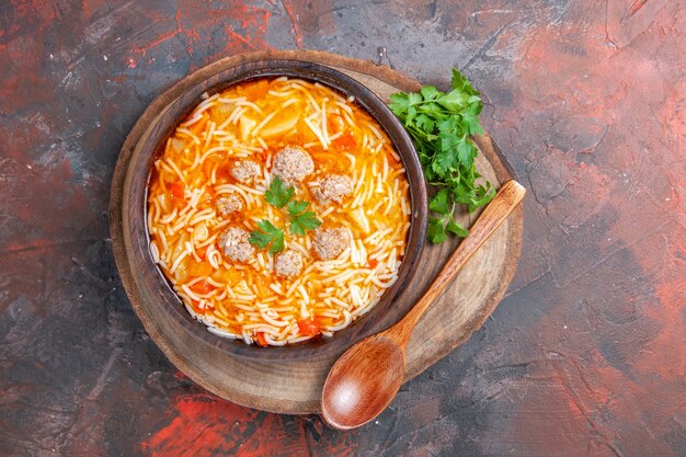 Close up view of delicious noodle soup with chicken and greens on wooden cutting board on dark background