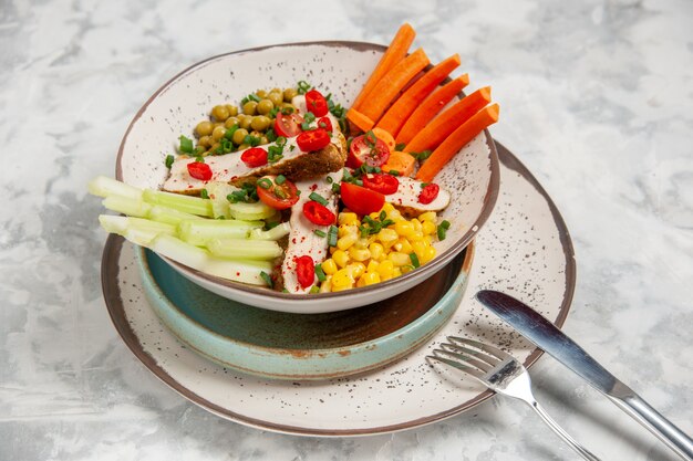 Крупным планом вид вкусного салата с различными ингредиентами на тарелке на подносах и столовых приборах на белой поверхности со свободным пространством