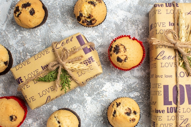 Vista ravvicinata di deliziosi piccoli cupcakes con cioccolato intorno a un regalo con iscrizione d'amore sulla superficie del ghiaccio