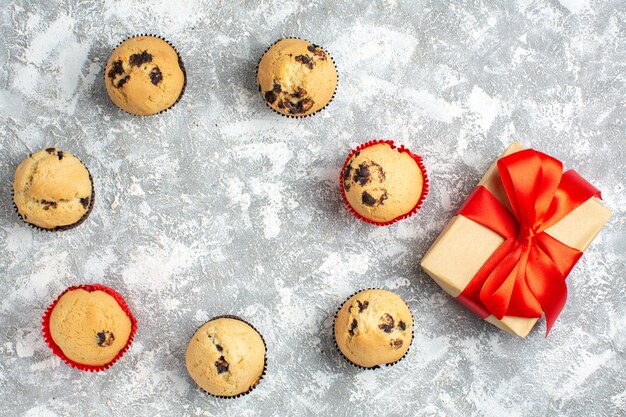 Close up view of delicious small cupcakes with chocolate and gift with red ribbon on ice surface