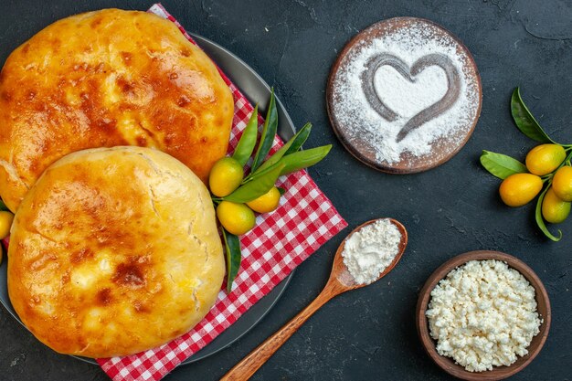 Close up view of delicous fresh baked pastries kumquats with stem on red stripped towel and cheese flour shaped in heart form on cutting board on dark blackground