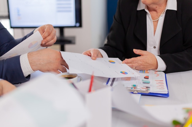 Close up view desk full of papers stats shown on charts and diverse businesspeople