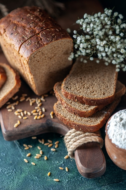 Close up view of dietary black bread wheats on wooden cutting board flower eggs flour in bowl on blue background