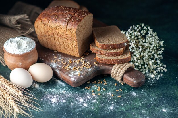 Close up view of dietary black bread wheats on wooden cutting board flower eggs flour in bowl on blue blurred background