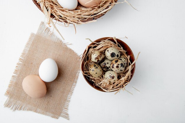 Close-up view of eggs on sackcloth and bowl of eggs in nest on white background with copy space