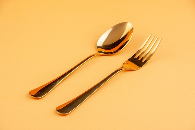 Free photo close up view of elegant shiny golden stainless spoon and fork on isolated yellow background with free space