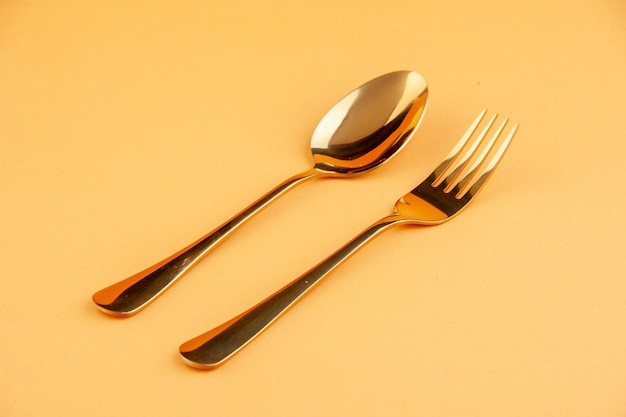 Close up view of elegant shiny golden stainless spoon and fork on isolated yellow background with free space