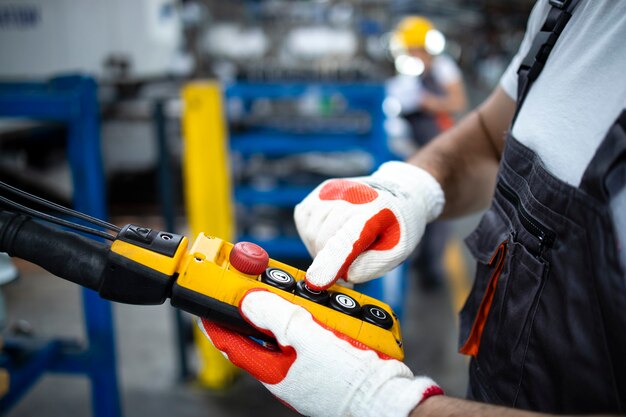 Close up view of factory worker operating industrial machine with push button joystick in production hall