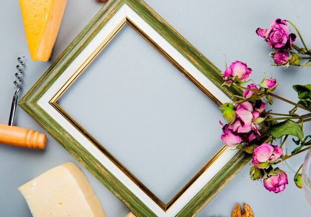 Close-up view of frame with cheese corkscrew and flowers around on white with copy space