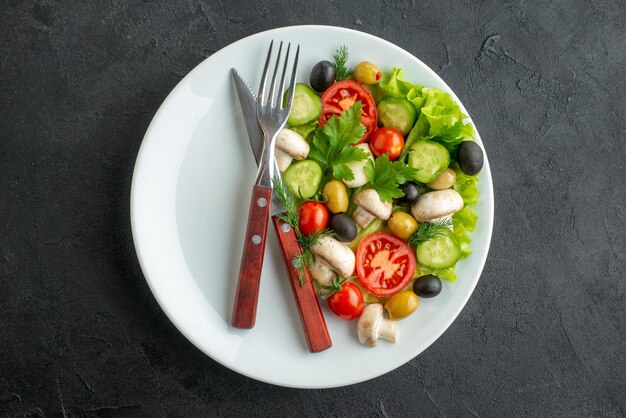 Close up view of fresh black and yellow olives chopped vegetables and cutlery set on a white plate on black background with free space